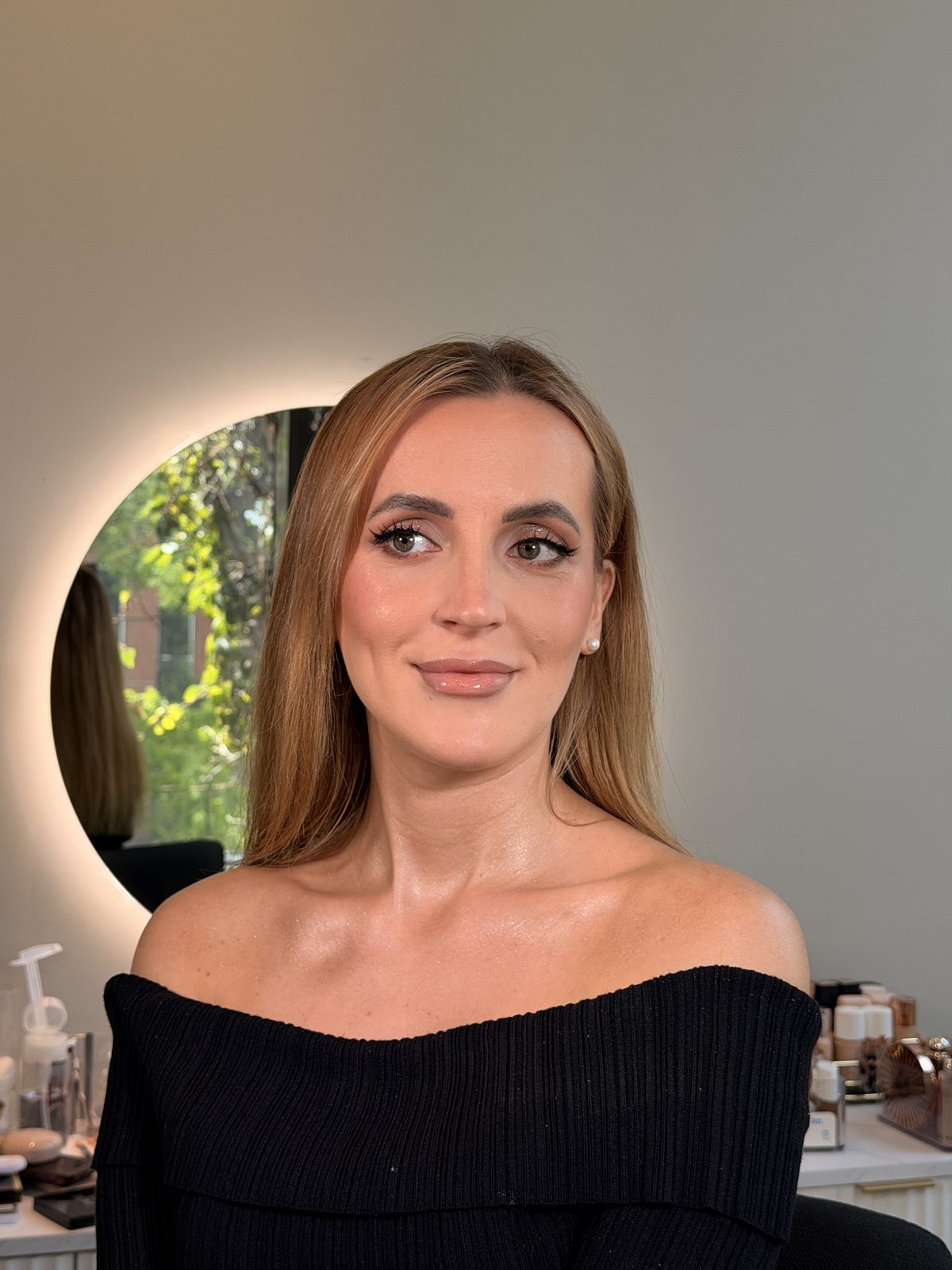 Evening makeup — defined eyes, glossy nude lip, sculpted highlight by the studio mirror